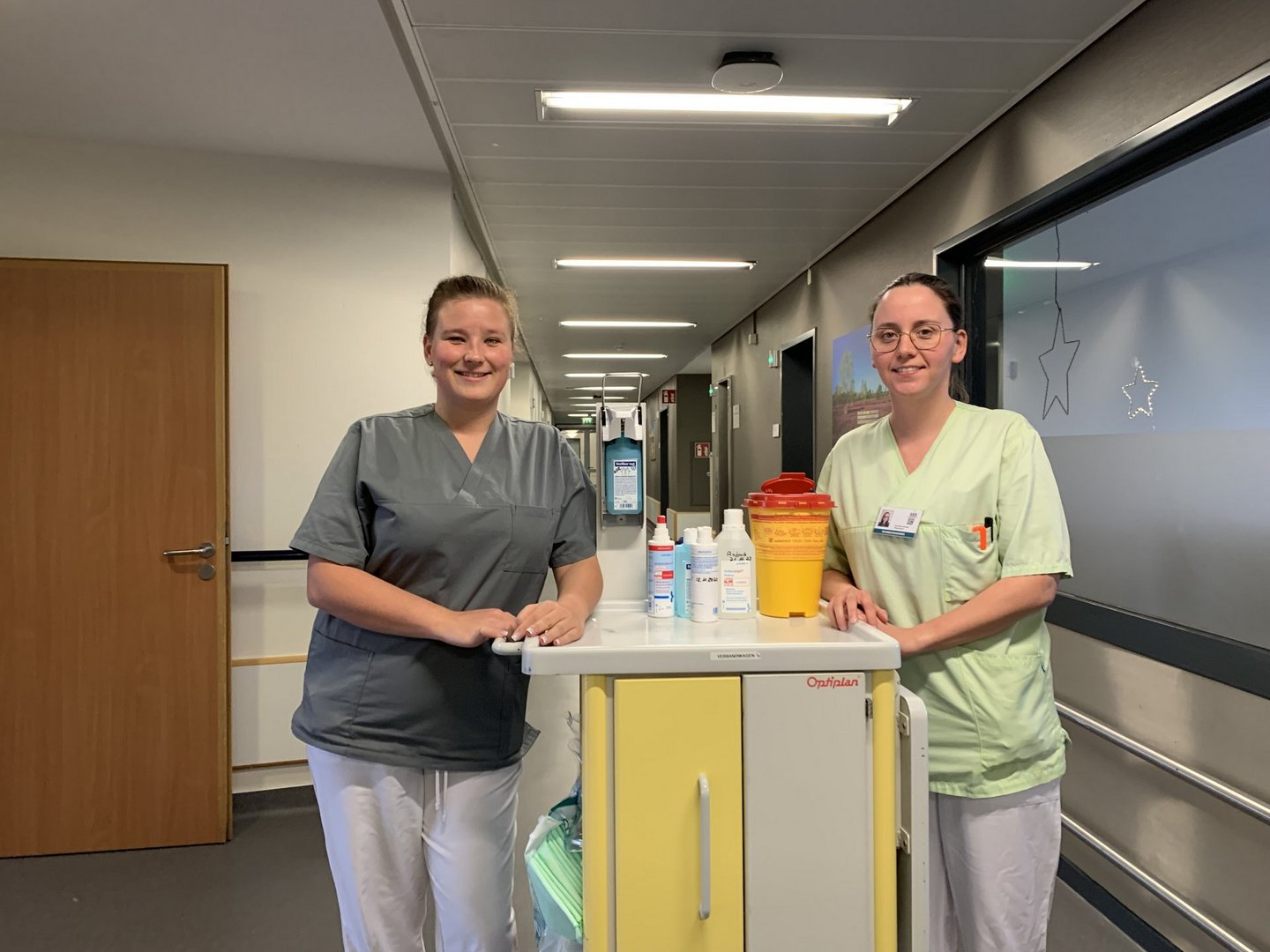 Zwei Pflegekräfte mit Hygiene- und Reinigungswagen im Klinikflur.
