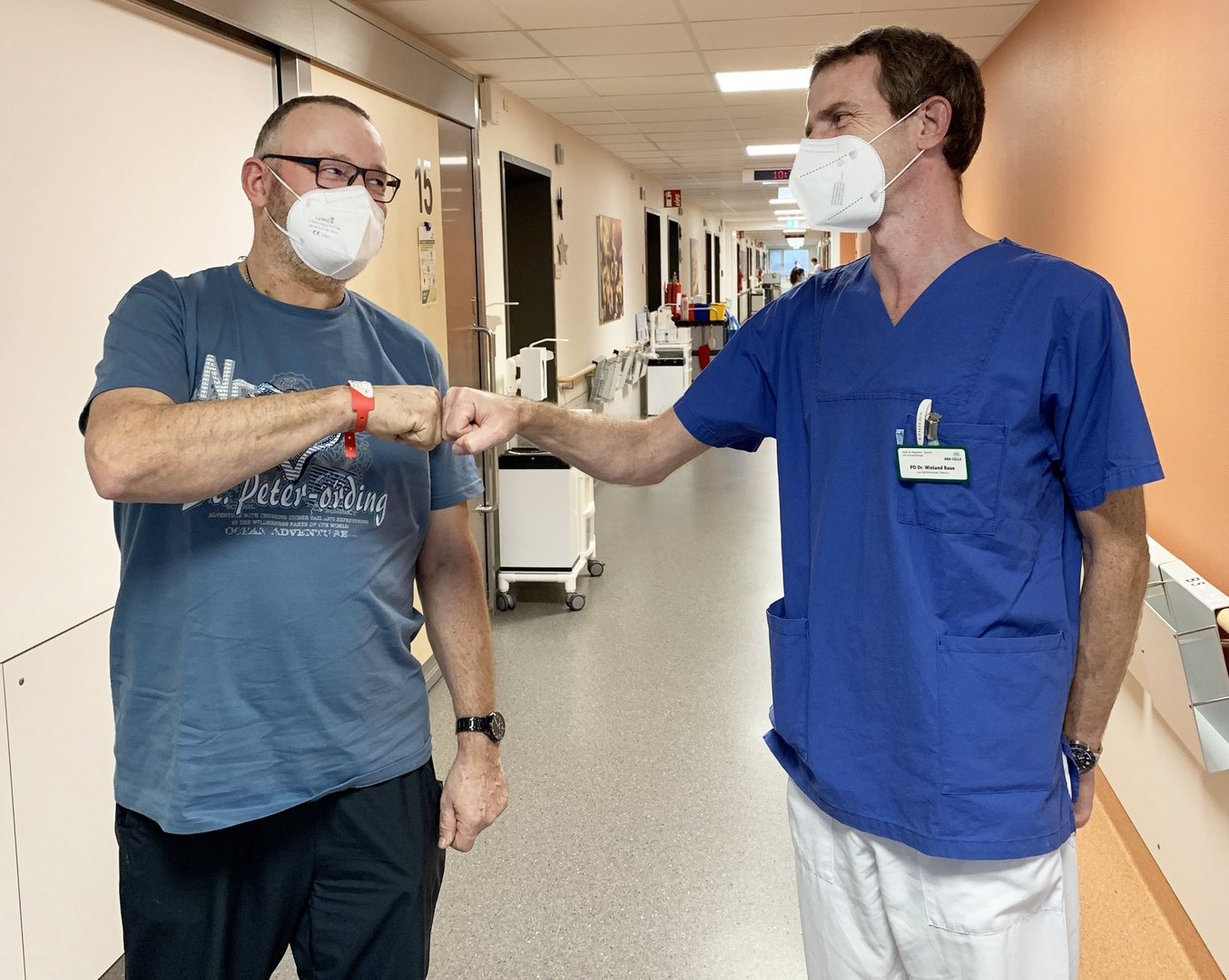Patient und Arzt begrüßen sich mit einem Faustgruß im Krankenhausflur