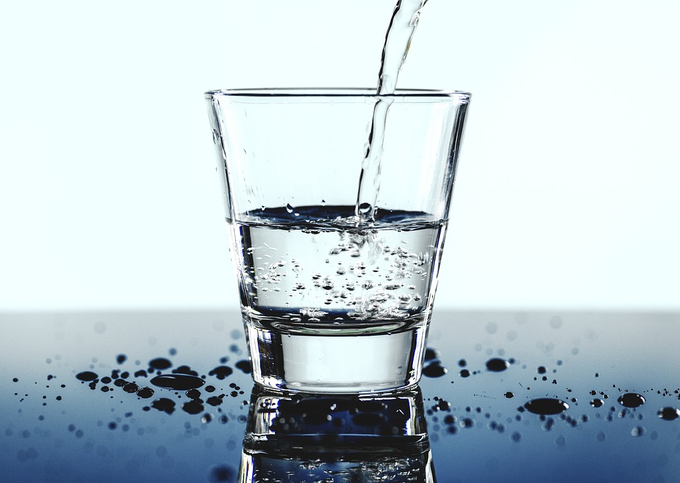 Ein Glas wird mit Wasser befüllt – Nahaufnahme auf spiegelnder Fläche